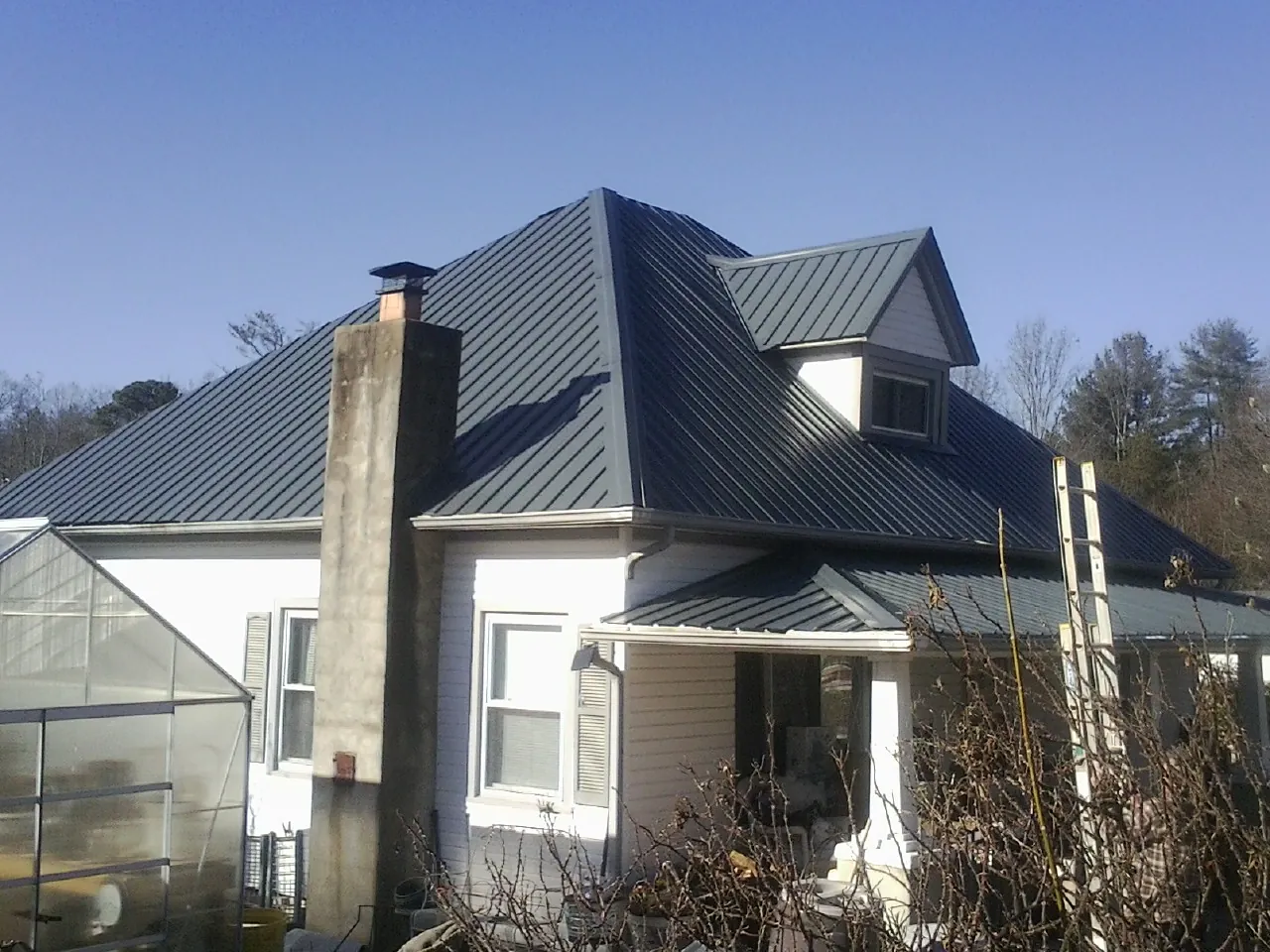 Dark blue standing seam metal roof on a white farmhouse with dormer — Slate & Tile Roof Repair by Roofing Brothers in Ulysses
